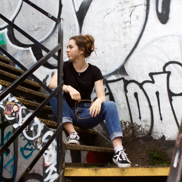 girl sitting on steps in front of graffiti wall